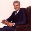 A man in suit and tie sitting on chair holding book.